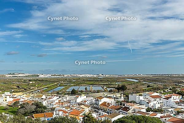 Wide panoramic view of Castro Marim showing traditional white houses with red roofs, streets, and surrounding countryside under a bright sky in the Algarve region of Portugal [IBR124586634]