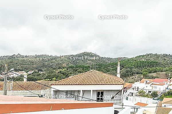 Panoramic view of São Marcos da Serra, a quiet rural village in the Algarve interior of Portugal, featuring traditional white houses, rolling green hills, and a cloudy sky [IBR124586640]
