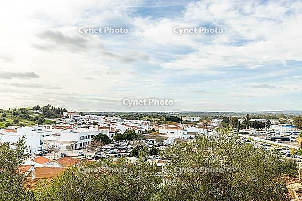 Wide panoramic view of Castro Marim showing traditional white houses with red roofs, streets, and surrounding countryside under a bright sky in the Algarve region of Portugal [IBR124586652]