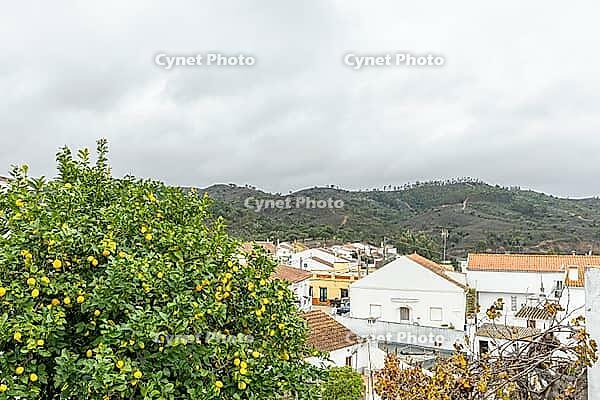 Lemon tree in the foreground with a view over São Marcos da Serra, a traditional village in the Algarve interior of Portugal, surrounded by hills, white houses, and cloudy skies [IBR124586663]