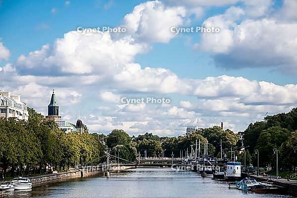 Turku, Finland - August 30, 2014 - Sunny riverfront scene with boats and bridge under cloudy blue sky [IBR124626852]