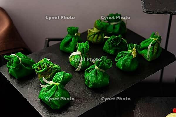 A selection of green pastry bites elegantly presented on a dark tray. these appetizing treats are wrapped and tied, adding a touch of sophistication to any culinary display [IBR124626873]