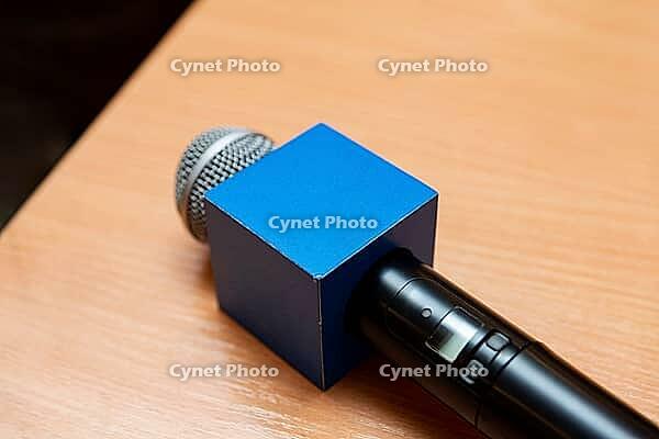 A close-up of a microphone featuring a distinctive blue square windscreen, resting on a wooden desk. ideal for media, broadcasting, or interview themes [IBR124626877]