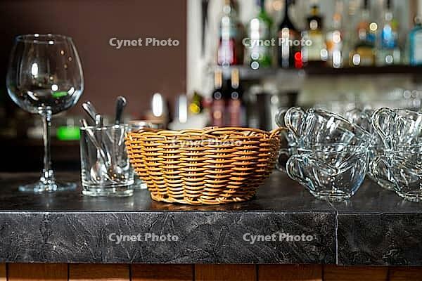 A stylish display of bar essentials on a dark countertop, featuring a wicker basket flanked by glassware and utensils. a glimpse of a well-stocked bar adds a touch of sophistication [IBR124626878]