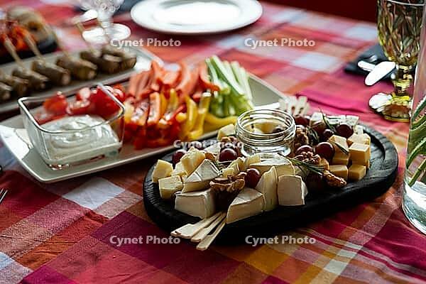 A beautifully arranged platter featuring an assortment of cheeses, fresh vegetables, and grapes. ideal for gatherings or parties, this setup combines color and flavor on a vibrant tablecloth [IBR124626880]