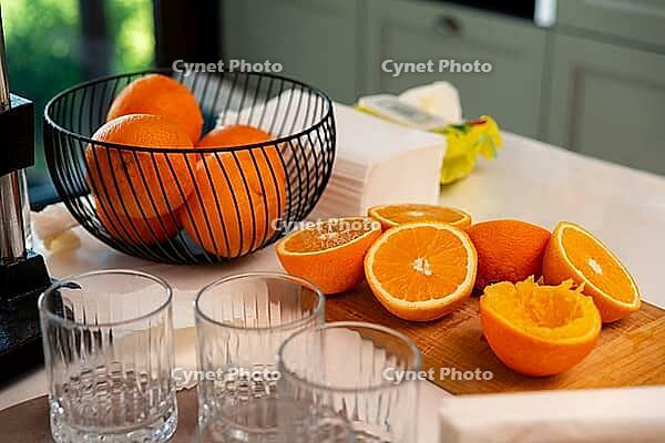 A kitchen counter displays fresh oranges, some sliced open beside a bowl, with glass tumblers ready for serving. the setting suggests a refreshing citrus beverage preparation [IBR124626881]