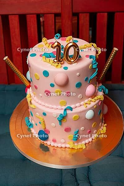 A vibrant two-tiered cake adorned with colorful polka dots and playful curly ribbons, topped with a golden number ten. perfect for a joyous tenth birthday celebration [IBR124626882]