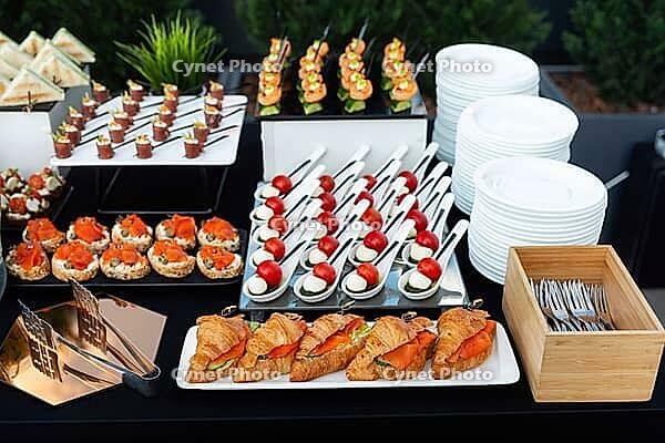 A meticulously arranged buffet showcasing a variety of appetizers including croissants, skewered tomatoes, bite-sized sandwiches, and more. ideal for events, parties, or gatherings [IBR124626883]
