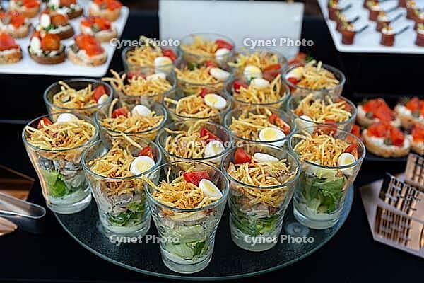 A sophisticated arrangement of appetizers in individual glasses, featuring a mix of fresh ingredients like greens, mini eggs, and toppings. ideal for catering events and sophisticated gatherings [IBR124626884]