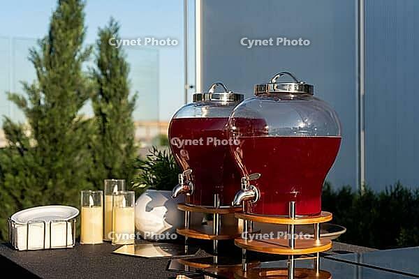 Two large glass dispensers filled with red juice are set up outdoors on a sunny day. the scene includes glasses and greenery, suggesting a refreshing outdoor gathering [IBR124626887]