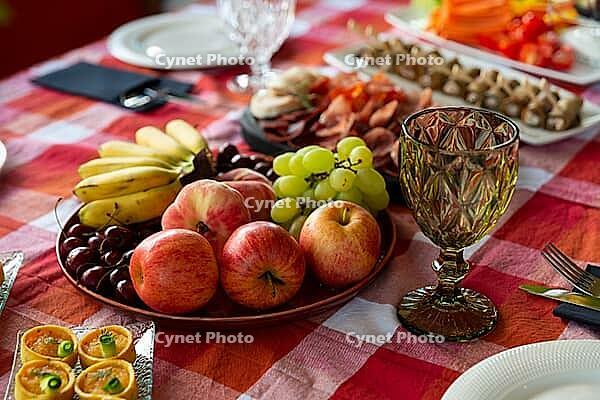A vibrant assortment of fresh fruits and savory appetizers arranged on a checkered tablecloth. the setting includes apples, grapes, cherries, and an elegant glass, perfect for gatherings [IBR124626890]