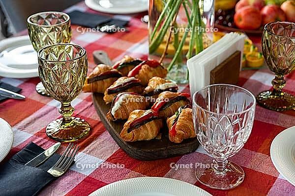 A well-set brunch table features croissants filled with fresh ingredients on a wooden board. crystal glassware and vibrant tablecloth add elegance and style to the setting [IBR124626891]