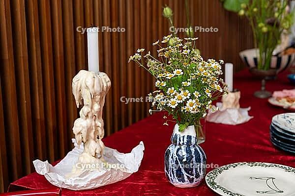 A stylish table setup featuring a tall candle with melted wax on a red cloth. a bouquet of white flowers in a blue vase adds a touch of charm to the scene [IBR124626914]