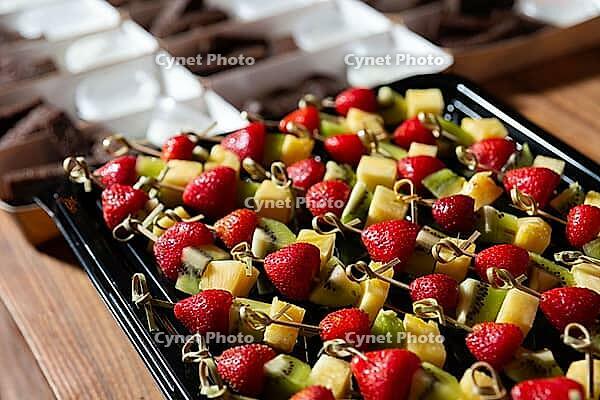 A vibrant display featuring skewers of fresh strawberries, kiwi, and pineapple, accompanied by chocolate desserts in the background. perfect for parties or gatherings [IBR124626918]