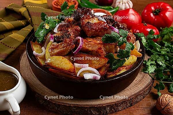 Ojakhuri, fried meat with potatoes, in ketsi, on a wooden table, Georgian cuisine, against a background of fresh ingredients [IBR124629125]