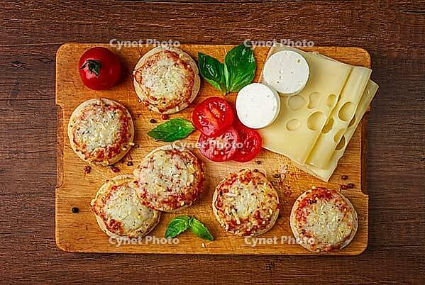 Freshly baked mini pizza, on a wooden board, with fresh vegetables and cheese, top view [IBR124748951]