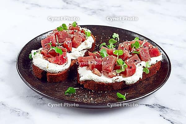 Sandwiches, rye bread with cream cheese, sliced tuna fillet with herbs, breakfast on a black plate, homemade [IBR124748959]
