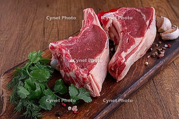 Freshly sliced lamb chops, with herbs and vegetables, on a wooden board, ready to cook, on a wooden table [IBR124748961]