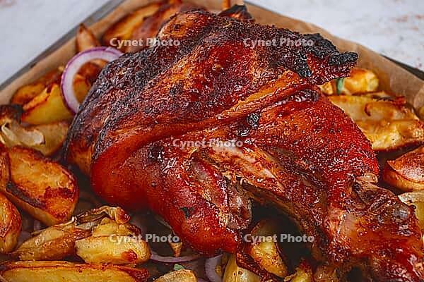 Baked pork knuckle, with potato slices, on a tray, with red sauce, homemade, no people, light background [IBR124748970]