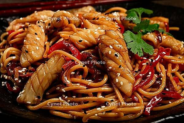 Udon noodles, with squid and vegetables, on a black plate, homemade, no people [IBR124748977]