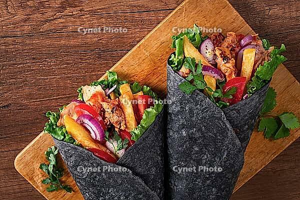Shawarma in black lavash, on a wooden background, chicken shawarma, no people [IBR124748978]