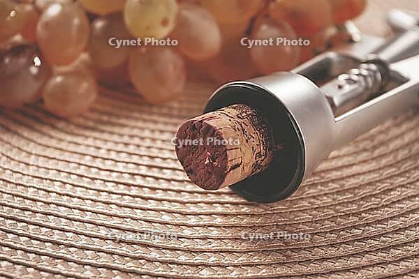 A corkscrew with a wine bottle stopper, lying on a woven napkin, with green grapes [IBR124748989]