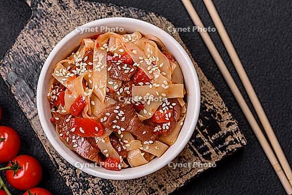 Food, Delicious asian udon dish with vegetables, meat, salt and spices on a ceramic plate on a dark concrete background [IBR124773704]