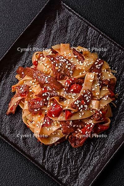 Food, Delicious asian udon dish with vegetables, meat, salt and spices on a ceramic plate on a dark concrete background [IBR124773705]