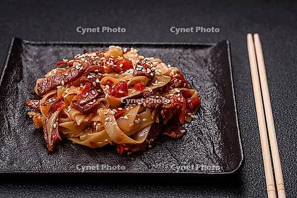 Food, Delicious asian udon dish with vegetables, meat, salt and spices on a ceramic plate on a dark concrete background [IBR124773707]
