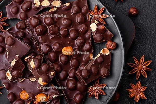 Food, Black bitter chocolate with whole hazelnuts, candied fruits and mint, broken into pieces on a dark concrete background [IBR124773710]