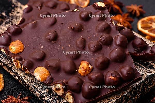 Food, Black bitter chocolate with whole hazelnuts, candied fruits and mint, broken into pieces on a dark concrete background [IBR124773711]