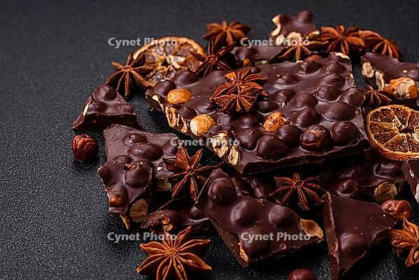 Food, Black bitter chocolate with whole hazelnuts, candied fruits and mint, broken into pieces on a dark concrete background [IBR124773713]