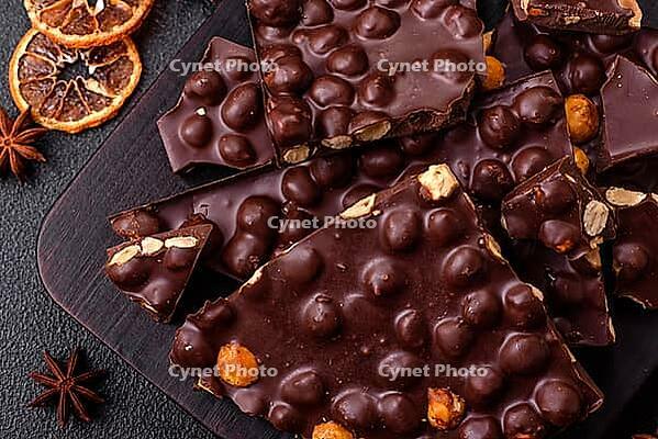Food, Black bitter chocolate with whole hazelnuts, candied fruits and mint, broken into pieces on a dark concrete background [IBR124773714]