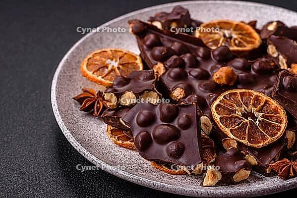 Food, Black bitter chocolate with whole hazelnuts, candied fruits and mint, broken into pieces on a dark concrete background [IBR124773715]