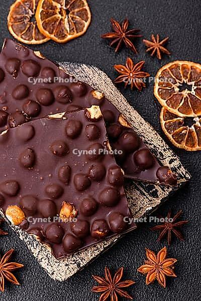 Food, Black bitter chocolate with whole hazelnuts, candied fruits and mint, broken into pieces on a dark concrete background [IBR124773716]