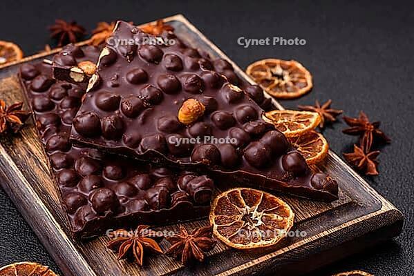Food, Black bitter chocolate with whole hazelnuts, candied fruits and mint, broken into pieces on a dark concrete background [IBR124773718]