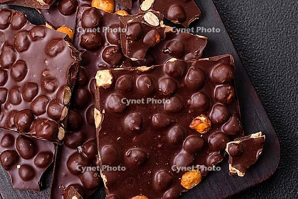 Food, Black bitter chocolate with whole hazelnuts, candied fruits and mint, broken into pieces on a dark concrete background [IBR124773719]