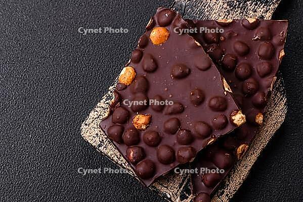 Food, Black bitter chocolate with whole hazelnuts, candied fruits and mint, broken into pieces on a dark concrete background [IBR124773720]