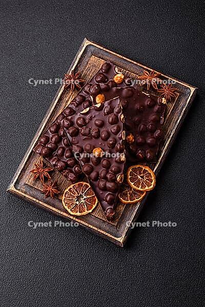 Food, Black bitter chocolate with whole hazelnuts, candied fruits and mint, broken into pieces on a dark concrete background [IBR124773721]
