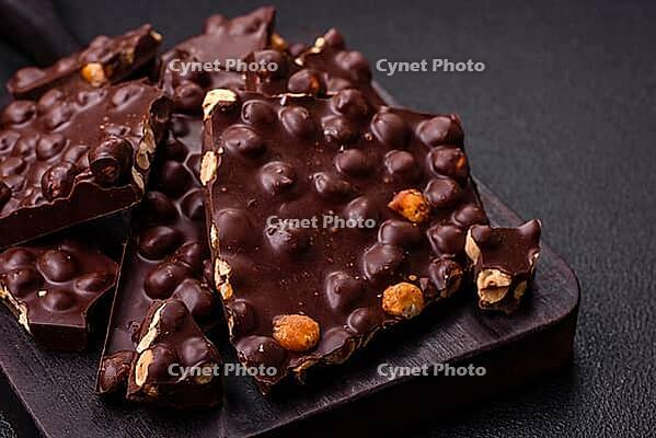 Food, Black bitter chocolate with whole hazelnuts, candied fruits and mint, broken into pieces on a dark concrete background [IBR124773722]