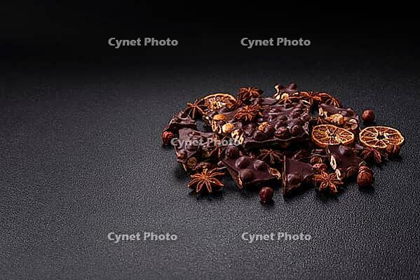 Food, Black bitter chocolate with whole hazelnuts, candied fruits and mint, broken into pieces on a dark concrete background [IBR124773723]