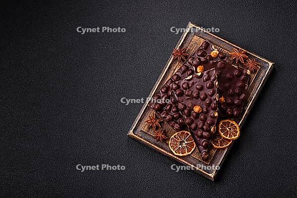 Food, Black bitter chocolate with whole hazelnuts, candied fruits and mint, broken into pieces on a dark concrete background [IBR124773724]