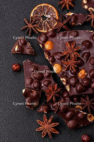 Food, Black bitter chocolate with whole hazelnuts, candied fruits and mint, broken into pieces on a dark concrete background [IBR124773726]