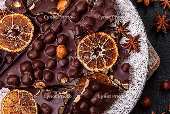Food, Black bitter chocolate with whole hazelnuts, candied fruits and mint, broken into pieces on a dark concrete background [IBR124773728]