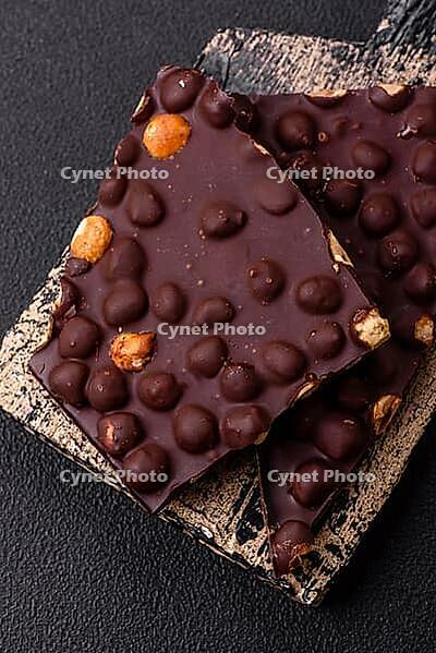 Food, Black bitter chocolate with whole hazelnuts, candied fruits and mint, broken into pieces on a dark concrete background [IBR124773730]