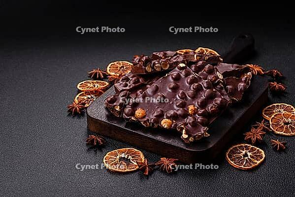 Food, Black bitter chocolate with whole hazelnuts, candied fruits and mint, broken into pieces on a dark concrete background [IBR124773733]