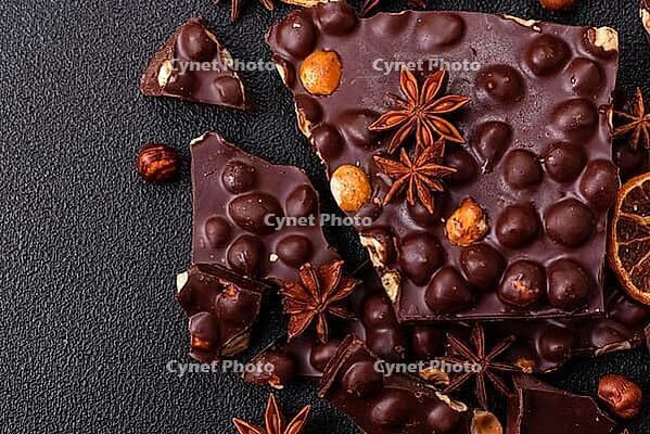 Food, Black bitter chocolate with whole hazelnuts, candied fruits and mint, broken into pieces on a dark concrete background [IBR124773734]