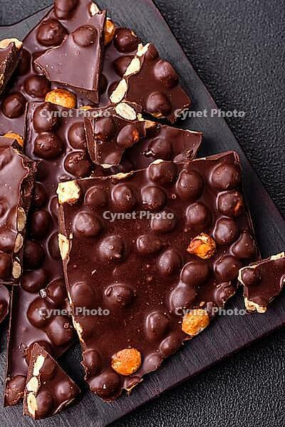 Food, Black bitter chocolate with whole hazelnuts, candied fruits and mint, broken into pieces on a dark concrete background [IBR124773735]
