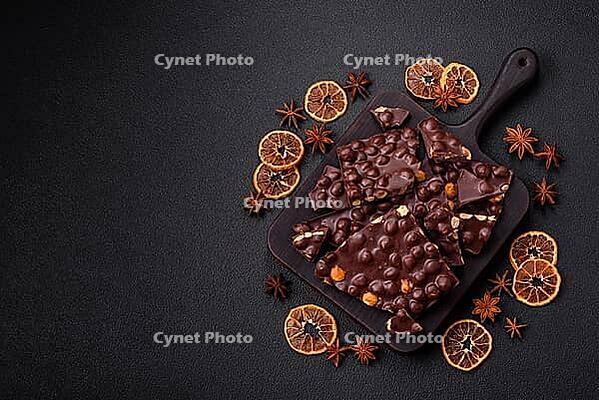 Food, Black bitter chocolate with whole hazelnuts, candied fruits and mint, broken into pieces on a dark concrete background [IBR124773736]