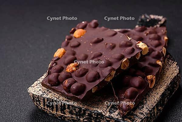 Food, Black bitter chocolate with whole hazelnuts, candied fruits and mint, broken into pieces on a dark concrete background [IBR124773739]